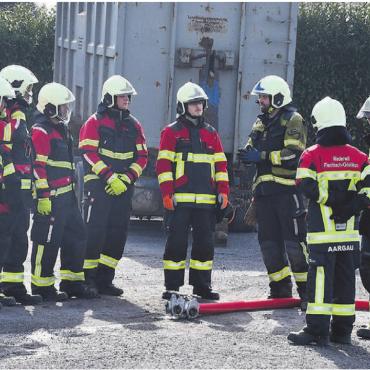 In das Handwerk eingeführt - Klassenlehrer Florian Berger, in der Mitte mit dunklem Anzug, instruiert die Gruppe von angehenden Feuerwehrleuten. Sie hören aufmerksam zu, bevor sie in Aktion treten. Denn überlegtes Handeln ist einer der Leitsätze, welche die Feuerwehr in ihrem Handwerk anstrebt. Bilder: Verena Anna Wigger