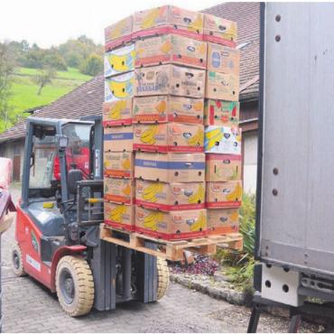 Hilfe für die Ärmsten - Mittels Gabelstapler werden die Bananenkisten in den Lastwagen gehievt. Dort packen weitere Helfer sie von der Palette weg.