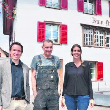 Dorfplatz optisch aufgewertet - Unter dem Wirtshausschild auf dem Dorfplatz: Gemeindeschreiber Lorenz Staubli mit Kunstschlosser Werner Villiger und Gemeinderätin Julia Huber (von links). Bild: Thomas Stöckli
