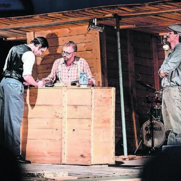 Ihm reicht ein Wort: Perfekt - Lonzi Müller (Philipp Galizia, Mitte) versucht als Unteragent der Auswandereragentur junge Männer zur Auswanderung nach Amerika zu bringen. Bild: Archiv / Gregor Galliker