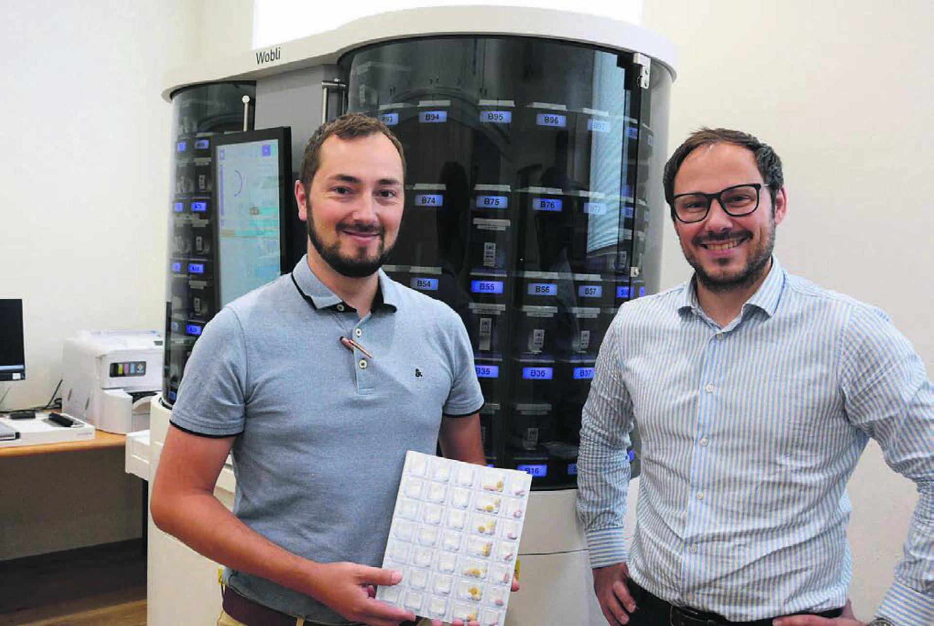Alain (links) und Pascal Jost mit ihrem neusten «Mitarbeiter», dem Dossierroboter VBM 200F, genannt Wobli. Er übernimmt in Zukunft das Bestücken der Wochenblister, wie ihn Alain Jost in der Hand hält. Bild: Chregi Hansen - Das Bild wird blockiert. – Möglicherweise durch einen aktiven Adblocker.