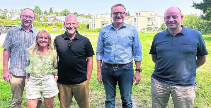 Auf dem Gelände rund um das Merkur-Areal im Hintergrund sollen die Festivitäten stattfinden. Diese fünf bilden einen Teil des OK der 850-Jahr-Feier 2028. Von links: Beat Koch, Romana Kammer, die beiden OK-Präsidenten Dennis Andermatt und Arsène Perroud – und Martin Laubacher. Bild: Stefan Sprenger