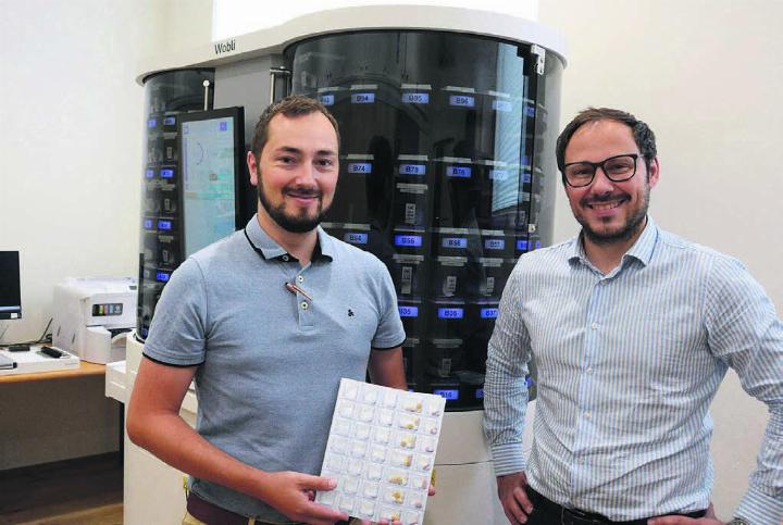 Alain (links) und Pascal Jost mit ihrem neusten «Mitarbeiter», dem Dossierroboter VBM 200F, genannt Wobli. Er übernimmt in Zukunft das Bestücken der Wochenblister, wie ihn Alain Jost in der Hand hält. Bild: Chregi Hansen